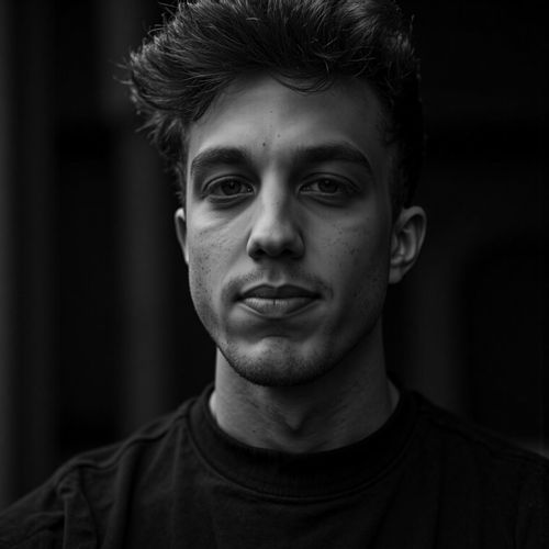 a black and white portrait of me MAN, close-up, with one half of their face in deep shadow. MAN looking intense.