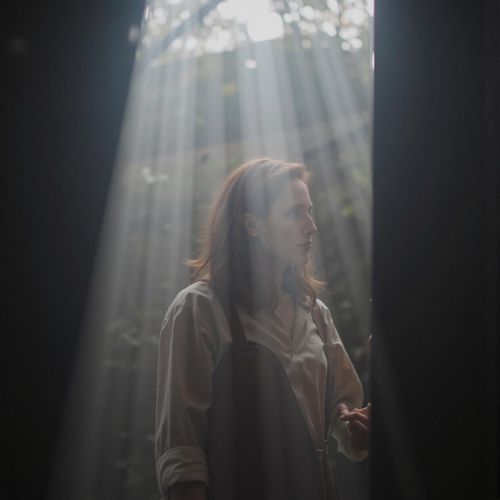 Showcase image for Film Noir - Prompt: a photo of me WOMAN in a smoky room, the light filtering through in beams, half body shot. WOMAN looking contemplative.