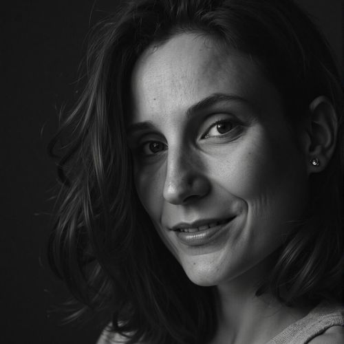 a black and white portrait of me WOMAN, close-up, with one half of their face in deep shadow. WOMAN looking intense.