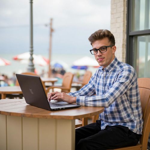 Showcase image for Remote Work Lifestyle - Prompt: a photo of me MAN working on a laptop at a beachside cafe, half body shot, looking focused but relaxed. MAN living the dream.