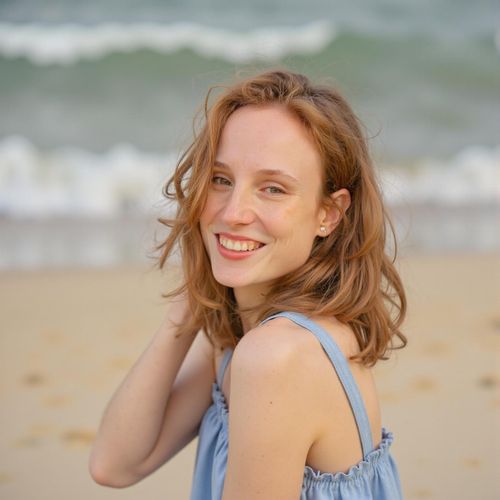 Showcase image for Beach - Prompt: a photo of me WOMAN at the beach, medium closeup, casual beachwear, friendly smile, sandy shore background, natural sunlight, ocean waves visible. WOMAN looking at the camera.
