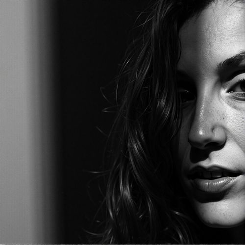 a black and white portrait of me WOMAN, close-up, with one half of their face in deep shadow. WOMAN looking intense.