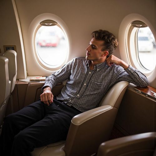 a photo of me MAN inside a luxurious private jet, half body shot, looking out the window with a contemplative smile. MAN exuding effortless success.