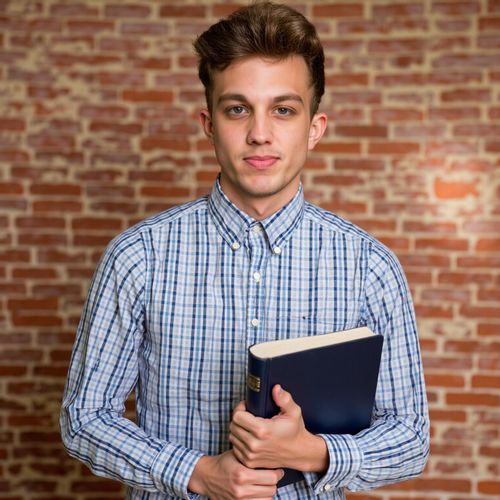 a photo of me MAN with a book subtly in hand, medium close-up, academic achiever yearbook photo. MAN looking intelligent and focused.
